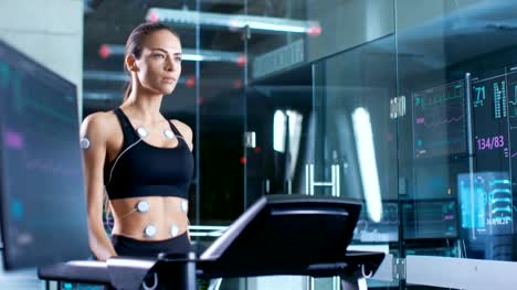 Beautiful-Woman-Athlete-Wearing-Sports-Bra-with-Electrodes-Connected-to-Her,-Walks-on-a-Treadmill-in-a-Sports-Science-Laboratory.-In-the-Background-Laboratory.-Medium-Shot.