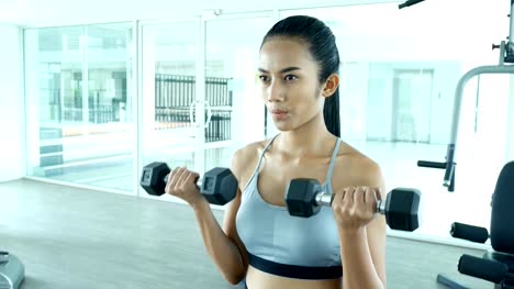 Sporty-young-asian-woman-exercising-with-dumbbells-in-the-gym.-Woman-exercise-at-fitness-gym.-Sport-and-Reaction-concept.-4k-Resolution.