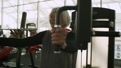 Mujer-Senior-entrenamiento-en-máquina-de-la-prensa-de-pecho-en-el-gimnasio
