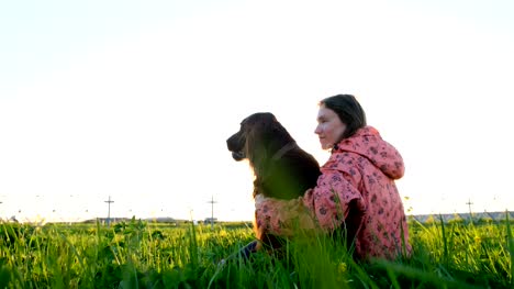 Woman-hugging-the-dog-at-sunset-while-sitting-on-the-grass
