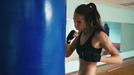 Hermosa-Kickboxing-de-raza-mixta-mujer-entrenamiento-saco-de-boxeo-en-la-feroz-fuerza-de-fitness-studio-fit-serie-de-kickboxer-de-cuerpo