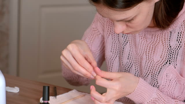 Frau-legt-zweiten-Mantel-Rosa-Schellack-auf-ihre-Nägel-und-reinigt-überschüssigen-Nagellack-mit-Holzstab-Orange-für-Maniküre.