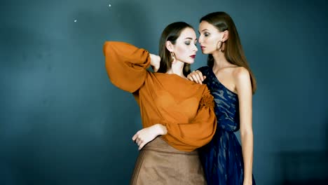 Modelle-zeigen-neue-Kleider,-berühmten-Damen-mit-hellen-Make-up-und-Ohrringe-in-Ohren-Nahaufnahme-zusammen-posieren-vor-der-Kamera-auf-dunkelblauem-Hintergrund