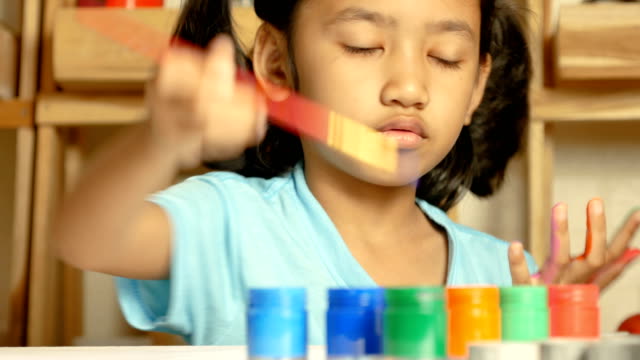 Das-kleine-Mädchen-nutzt-einen-roten-Pinsel-eingetaucht-in-einer-farbigen-Flasche-an-ihrem-Finger-zu-malen.
