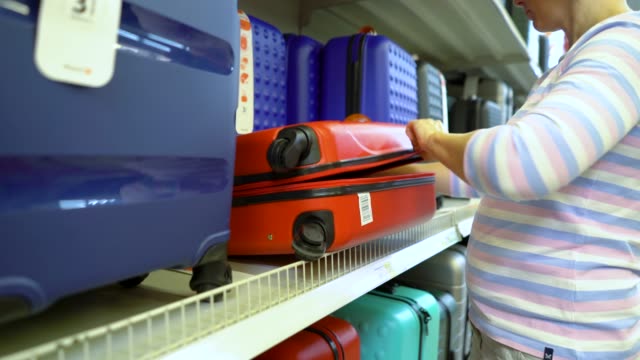 Caucasian-woman-near-shop-shelves-choosing-suitcase-in-haberdashery-market