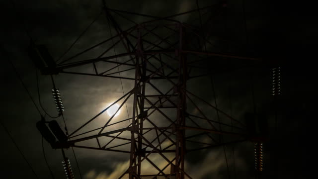 the-moon-in-the-cloudy-sky,-visible-through-the-power-line-support,-time-lapse.
