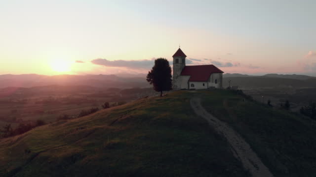 Enthüllen-schießen-einer-katholischen-Kirche-auf-einem-Hügel-mit-einem-wunderschönen-Blick-auf-das-Dorf-im-Sommer-in-den-Sonnenuntergang