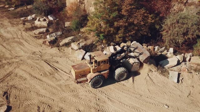 professionelle-Bulldozer-mit-einem-Eimer-breitet-sich-Sand-in-der-Nähe-von-den-Steinen-auf-dem-Hintergrund-des-Steinbruchs.