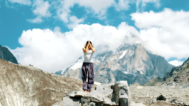 Junge-Frau-führt-eine-grundlegende-Krieger-Asana-Yoga-vor-dem-Hintergrund-der-schneebedeckten-Berg-in-der-Wanderung.-Mädchen-macht-Turnen-und-Gymnastik-an-der-frischen-Luft-bei-einer-Wanderung-auf-die-Natur