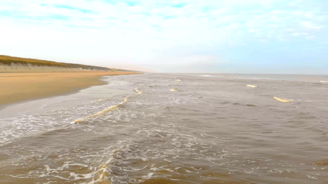 Aerial-view.-Slow-motion-flight-over-the-sea-and-the-waves-that-arrive-to-shore-in-the-sunny-morning.-Netherlands-Zandvoort.-North-Sea.-Shore-line