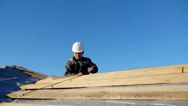 Erwachsenen-professionelle-Bauunternehmer-in-Bauarbeiterhelm-Messlänge-Holz-lumber-vor-Ort-unter-blauem-Himmel,-Slow-motion