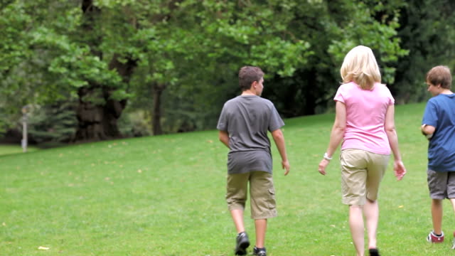 Zwei-Jungs-im-Teenageralter-Spaziergang-in-einem-Park-mit-ihrer-Mutter.