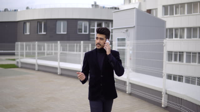 Serious-handsome-young-businessman-communicating-on-smartphone-smiling-confident.