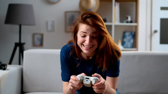 Determined-girl-playing-a-video-game-at-home.-Excited-gamer-woman-sitting-on-a-couch,-playing-and-losing-in-video-games-on-a-console,-using-a-wireless-controller.-Cozy-room,-lovely-home-atmosphere
