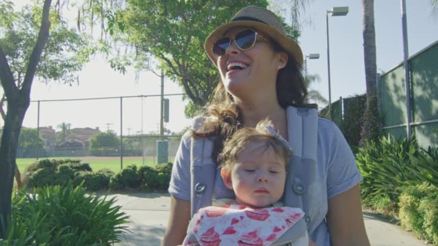 Frau-mit-einem-Baby-in-Träger-lächelnd,-wie-sie-in-einem-Park-geht