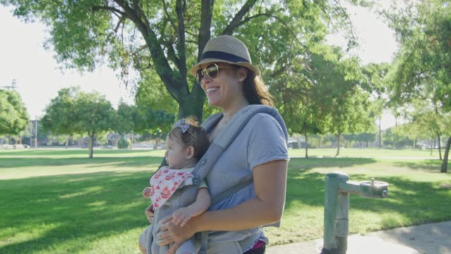 Happy-woman-walking-on-a-park-carrying-her-baby-on-carrier