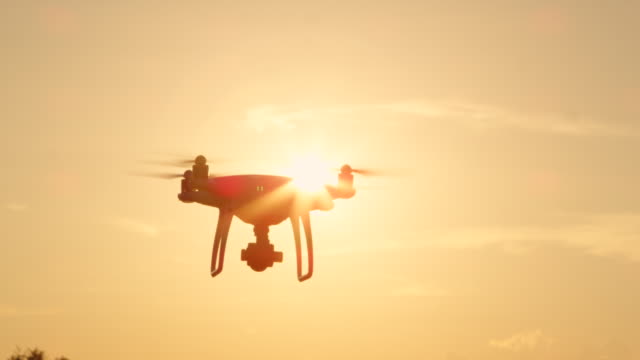 CLOSE-UP-LENS-FLARE-SILHOUETTE:-Dreharbeiten-Drohne-mit-Kamera-über-goldene-Sonne-fliegen