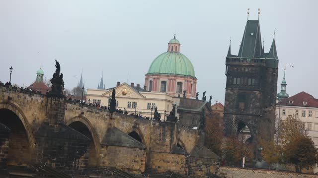 The-Charles-Bridge-on-the-background-of-the-old-tower-and-the-green-dome-of-the-cathedral-in-Prague,-side-view,-tourists-stroll-along-the-Charles-Bridge,-Prague,-October-19,-2017