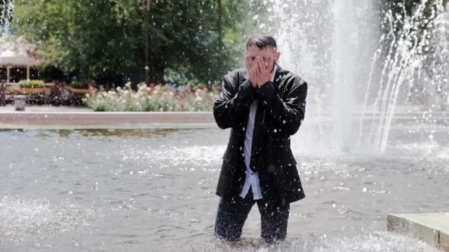 A-man-is-walking-in-a-fountain,-covering-his-face-with-hands-and-feeling-all-the-sadness-in-the-world