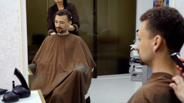 Hairdresser-cuts-hair-of-handsome-man-with-electric-razor