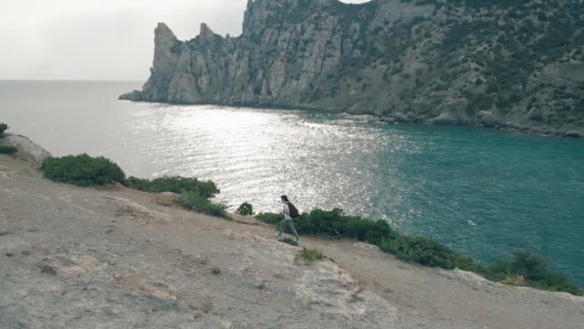 Mujer-vista-aérea-camina-en-contra-del-océano-y-las-rocas