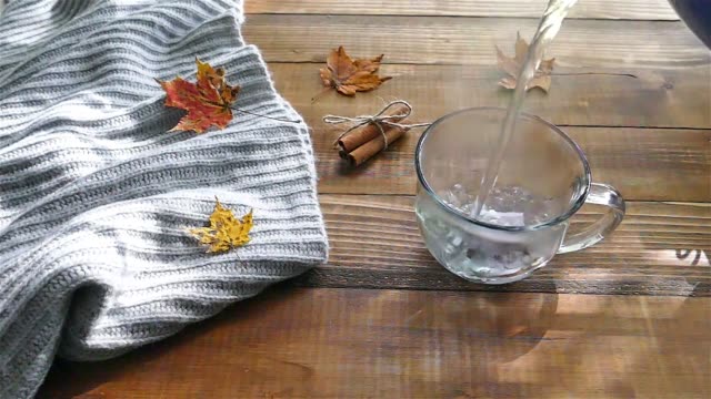 Pouring-water-to-cup-with-a-tea-bag-on-a-wooden-table-with-colored-autumn-leaves---slow-motion