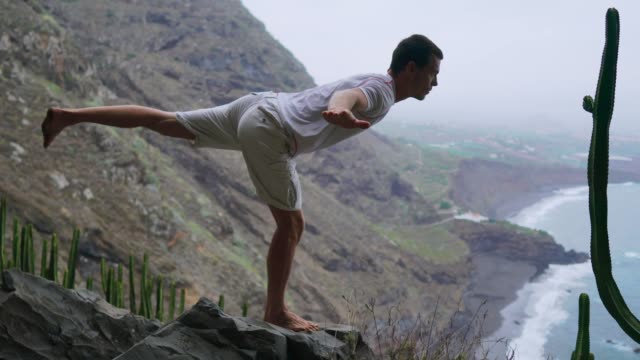 Fit-young-man-practices-sun-salutation-yoga-in-mountain-for-ocean.-Young-man-enjoying-meditation-and-yoga.-fitness,-sport,-people-and-lifestyle-concept---young-man-making-yoga-exercises.