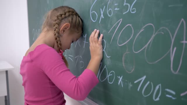 unglücklich-Schulmädchen-in-der-Nähe-von-Board-mit-Beispielen-zur-Mathematik-in-der-Grundschule-Klasse