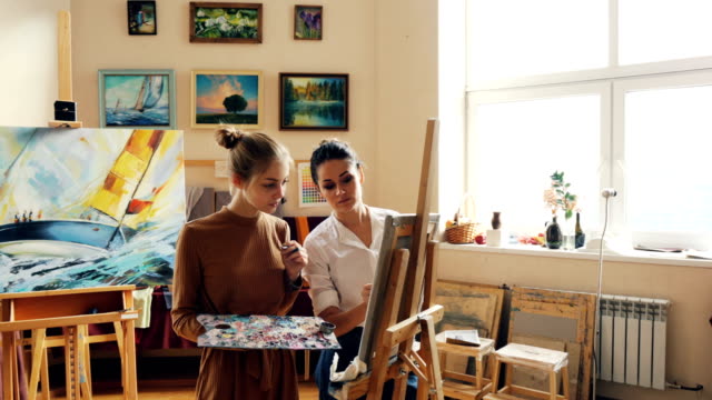 Gut-aussehende-Mädchen-lernt-malen-mit-Klasse-mit-erfahrenen-Lehrerin-geschickten-Maler,-Menschen-arbeiten-und-reden,-diskutieren-bildende-Kunst.