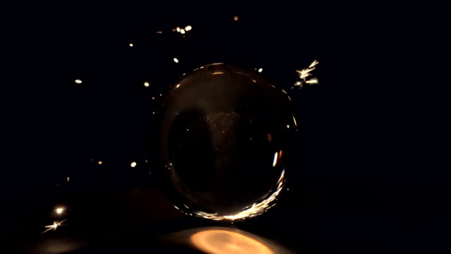 Burning-sparkler-behind-a-glass-ball-on-a-black-background.