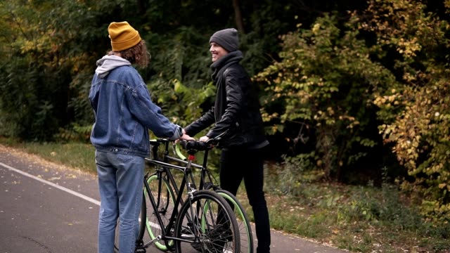 Schöne-junge-Paar-umarmt,-beginnend-mit-Fahrrädern-im-Stadtpark-im-Herbst-Park-zu-gehen.-Konzept-der-aktiven-Lebensstil,-Kommunikation,-dating.-Seltener-Blick