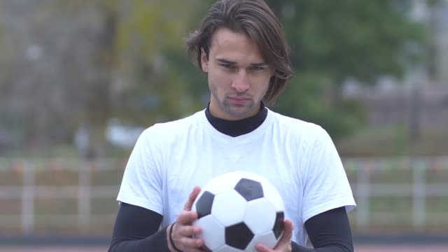 Portrait-of-a-young-guy-in-a-sports-t-shirt-holding-a-soccer-ball-in-his-hands-and-strictly-looking-at-the-camera-Sports-guy-with-a-ball-in-his-hands-with-a-cheeky-look