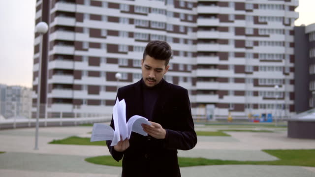 Attractive-young-businessman-in-black-suit-throw-out-documents-outdoor-against-office-building.