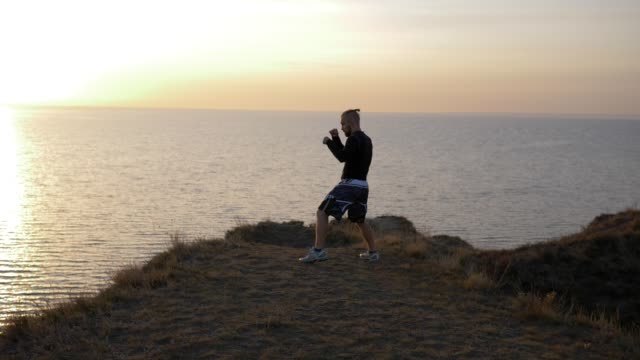 sports-activities,-muscular-boxer-guy-fulfills-blows-before-championship-on-hill-near-sea