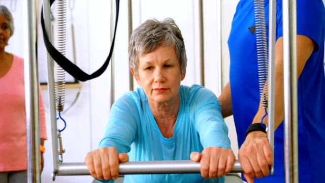 Trainer-unterstützen-ältere-Frau-bei-der-Ausübung-von-Yoga-4k