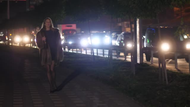 A-girl-in-a-short-skirt-goes-along-the-night-road-and-drinks-wine-from-the-bottle-4K-Slow-Mo