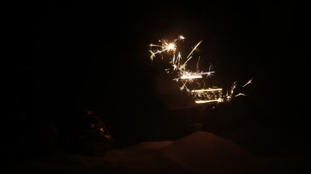 Glittering-burning-sparkler-on-snow-with-blurred-Christmas-tree-on-dark-background.-New-Year-Holiday-concept-with-empty-space-for-your-text.-Selective-focus