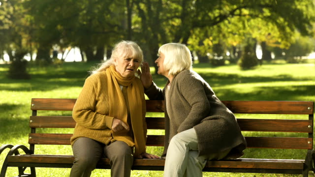 Old-women-telling-secrets,-sitting-on-bench-in-park,-friendship,-golden-years