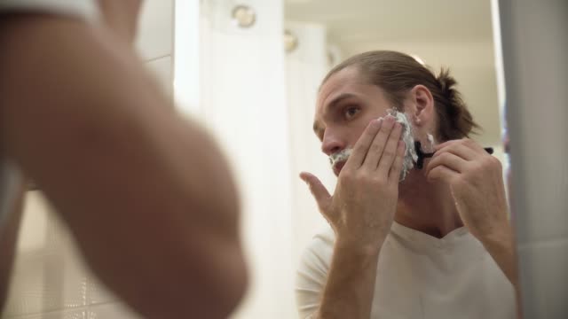 Man-Shaving-Beard-With-Razor-In-Bathroom