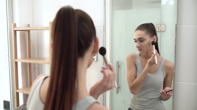 Face-Makeup.-Woman-Using-Powder-And-Looking-In-Mirror