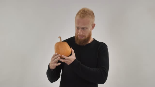 Redhead-guy-holding-pumpkin,-preparing-for-Halloween