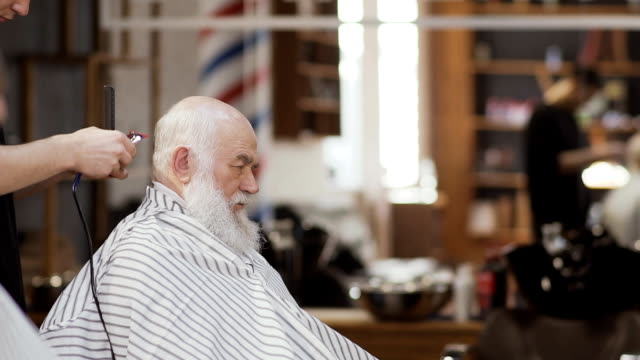Friseur-macht-stilvolle-Frisur-für-reifer-Mann-im-barbershop