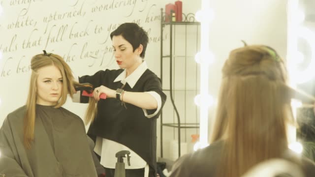Hairdresser-making-hairstyle-with-hair-tongs-and-comb-for-hair-straightening-in-beauty-salon.-Close-upfemale-hairdresser-straightening-long-hair.-Woman-hairstyling-in-hairdressing-salon