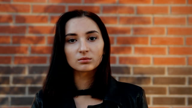 Portrait-of-a-young-serious-sexy-woman-against-a-brick-wall.-Slow-motion-shot.