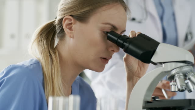 Mujer-utilizando-microscopio-y-hablando-con-el-colega
