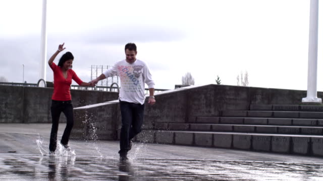 A-couple-runs-and-jumps-through-the-puddles-of-a-fountain-in-a-park