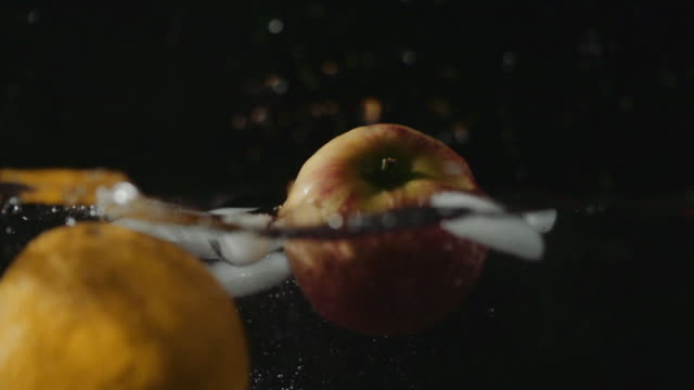Naranja,-manzana-y-caída-de-cubos-de-hielo-en-el-agua