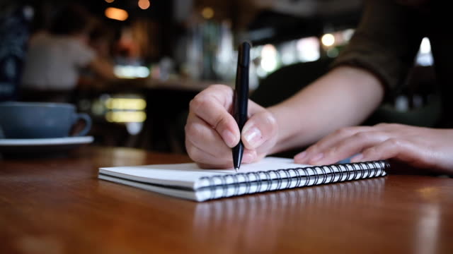 Slow-Motion-von-Frauenhand-schreiben-auf-leere-Notebooks-auf-Holztisch-im-café