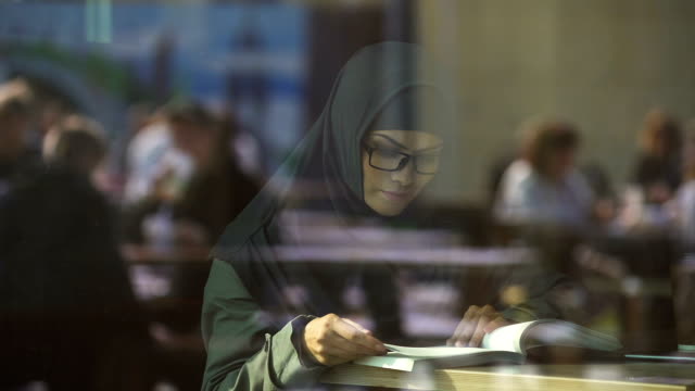 Libro-de-lectura-de-la-señora-joven-árabe-en-café,-preparación-para-exámenes-de-estudiante