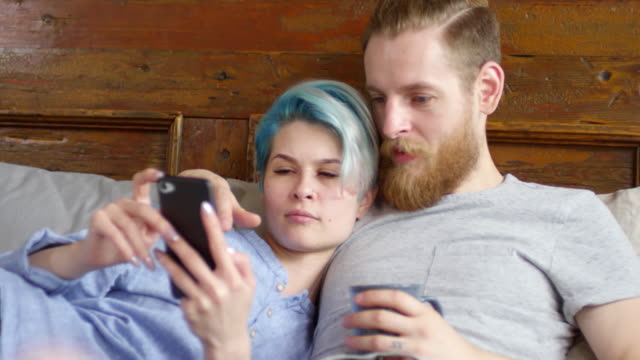 Hipster-Couple-with-Mobile-Phone-Relaxing-on-Bed